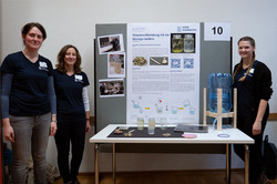 Drei Studentinnen der HAW Hamburg stellen mit einem Poster und einem Wassertank ihr Projekt zur Wasseraufbereitung vor.