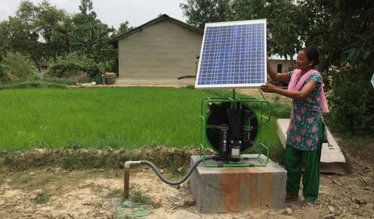 Eine Frau steht neben einer solarbetriebenen Wasserpumpen für Einzelhaushalte