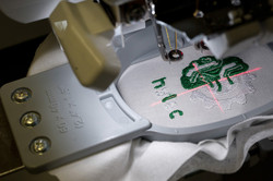 Auf einer Stickmaschine wird das Logo des Projektes HyLeC auf ein Stück weißen Stoff gestickt.
