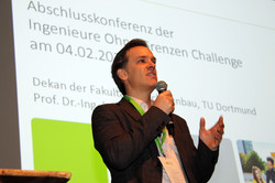 Der Dekan der Fakultät Maschinenbau steht mit einem Mikrofon in der Hand auf der Bühne und Begrüßt die Anwesenden.