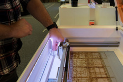 Ein aufgeklappter Lasercutter, in dem eine Holzplatte liegt.