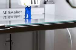 Der Innenraum eines laufenden 3D-Druckers, in dem eine kleine blaue Figur entsteht.