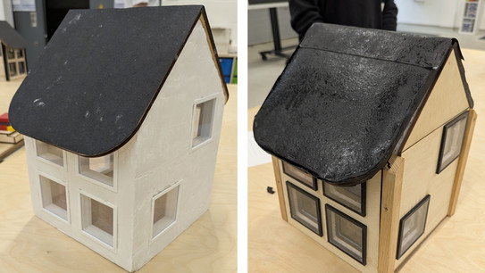 Ein Foto mit zwei Modellhäuserm. Die Dächer sind mit Dachpappe beklebt, in den Fensterausschnitten kleben Scheiben aus Plexiglas. Das Haus links ist mit Gips weiß verputzt, das Haus rechts hat eine Holzfassade.