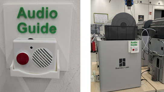 Links im Bild ich ein kleiner weißer Lautsprecher zu sehen, auf dem sich ein roter Knopf befindet. Der Lautsprecher steckt in einer weißen Halterung mit der Aufschrift "Audio Guide". Rechts im Bild ist ein 3D-Drucker fotografiert. An der Seite des Gerätes befindet sich einer dieser kleinen Lautsprecher.