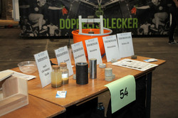 Auf einem Tisch stehen Gefäße mit unterschiedlich stark verschmutztem Wasser. Dahinter stehen Schilder, auf denen Filterstufen erklärt werden.