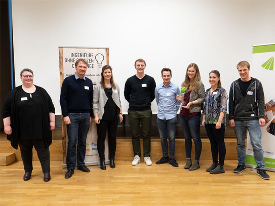 Eine Gruppe von 5 Studierenden wird als Sieger ausgezeichnet. Eine Studentin hält einen Pokal in der Hand. Daneben stehen zwei Lehrende und ein Vertreter von IoG.