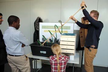 Ein Student demonstriert die Funktion eine Modells, mit dem Wasser in einen Filterkasten transportiert wird. Zwei Studierende schauen dabei zu.